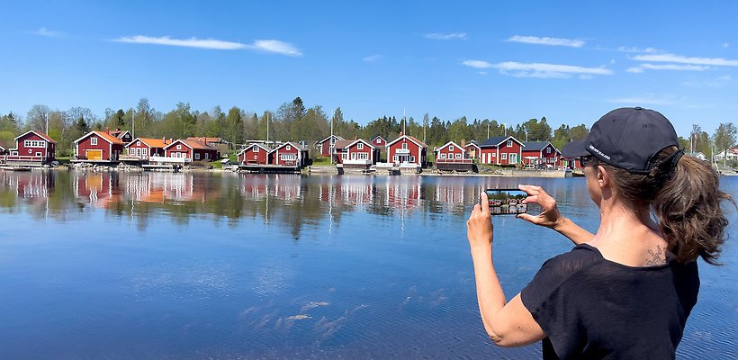 En person fotografera röda hus vid en havskust med sin mobil. Fotograf: Bert Öhman.