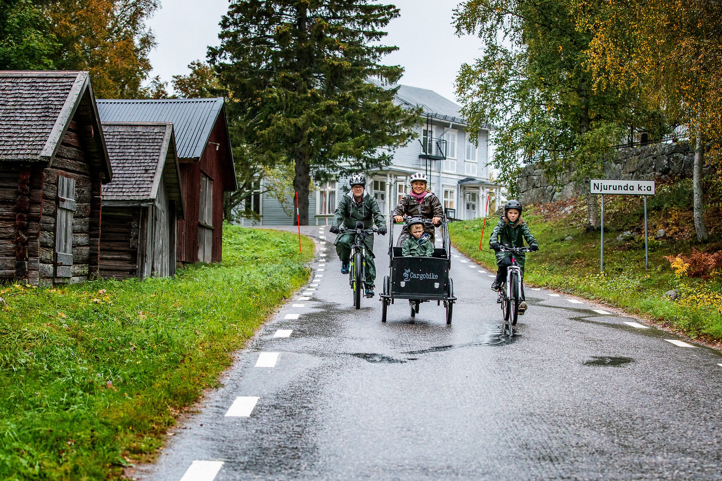 Alttext: En familj cyklar ute i regnet Fotograf: Therese Ny Bildtext: Familjen Persson-Eriksson i Njurundabommen testar under hösten det bilfria livet i så hög utsträckning som möjligt. 